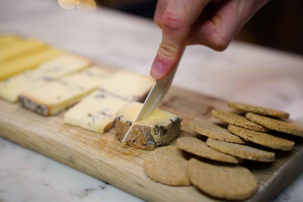 A close-up of hands cutting artisanal cheese on a wooden board at a cheesemonger.